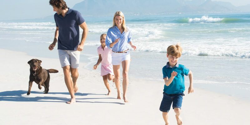 A Healthy Family And Their Dog Running On The Beach.